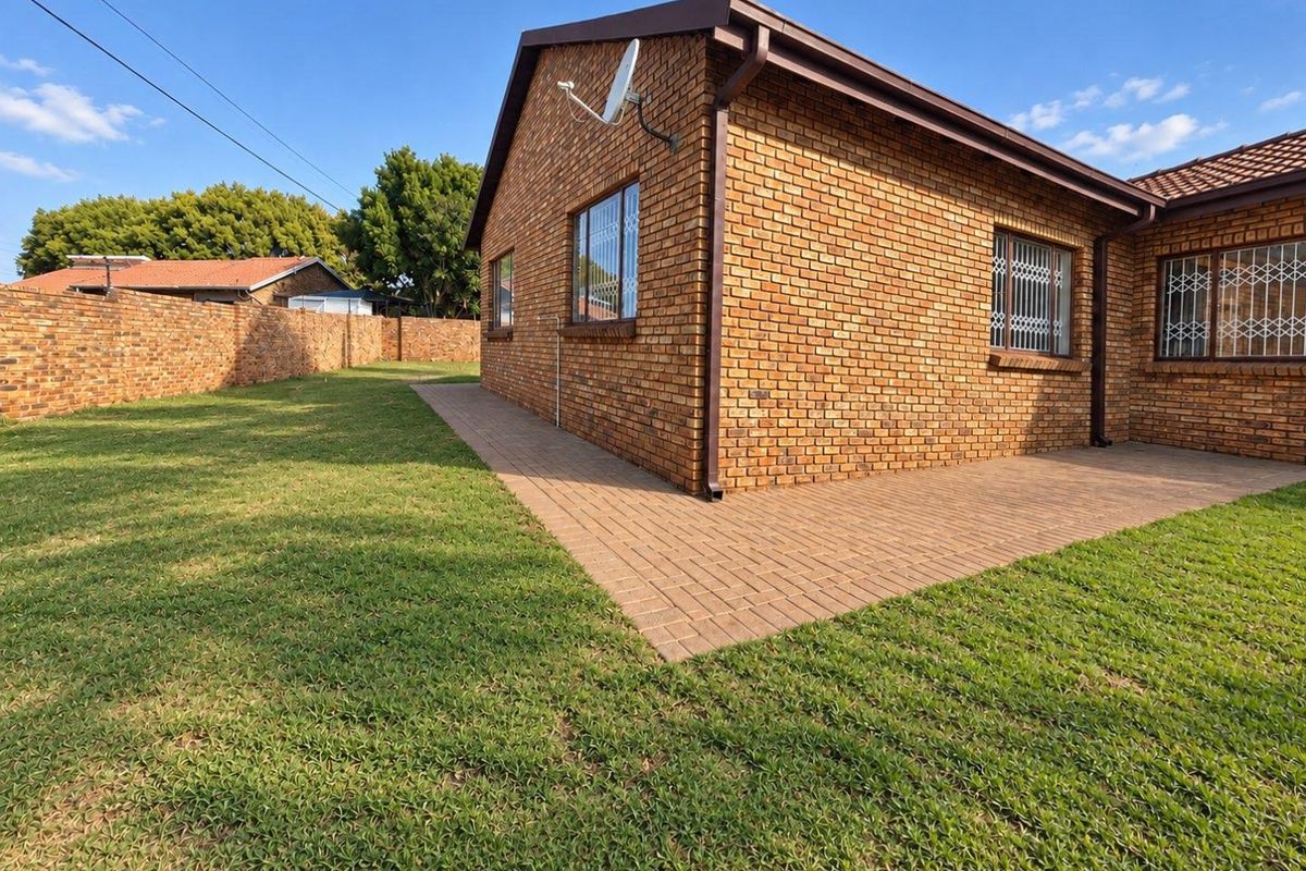 A view of the rear exterior featuring face brick walls, a paved patio area, and a well-maintained lawn enclosed by a brick boundary wall.