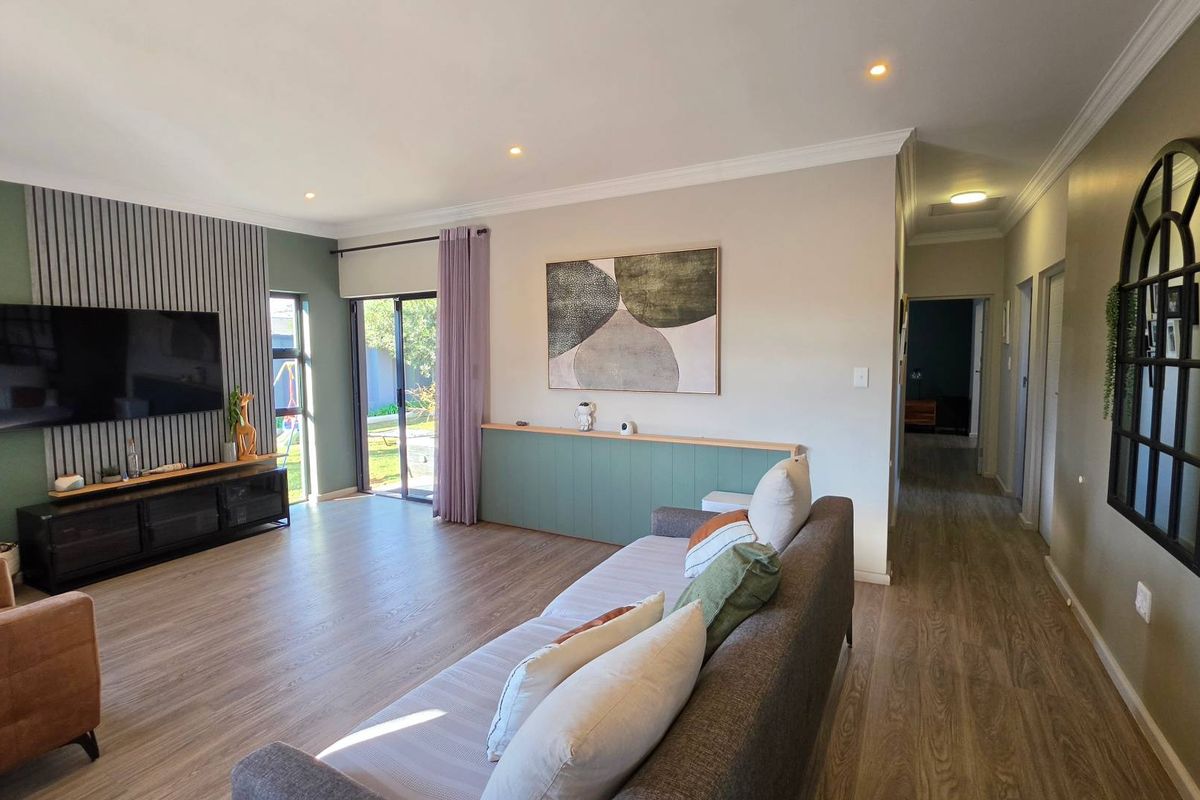 Spacious living room featuring modern laminate flooring, a stylish slatted feature wall, recessed downlighting, and direct access to the garden through sliding glass doors.