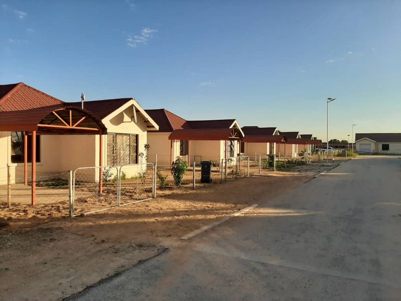 A row of residential houses featuring tiled roofs, covered carports, and wire fencing in a developing neighborhood setting.