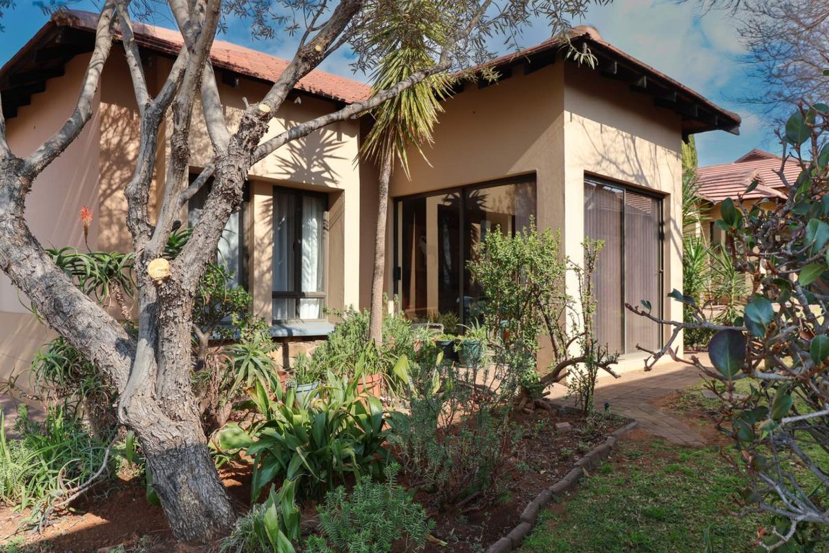 A view of the rear exterior of the retirement unit, featuring a paved patio area, sliding glass doors, and established garden landscaping.