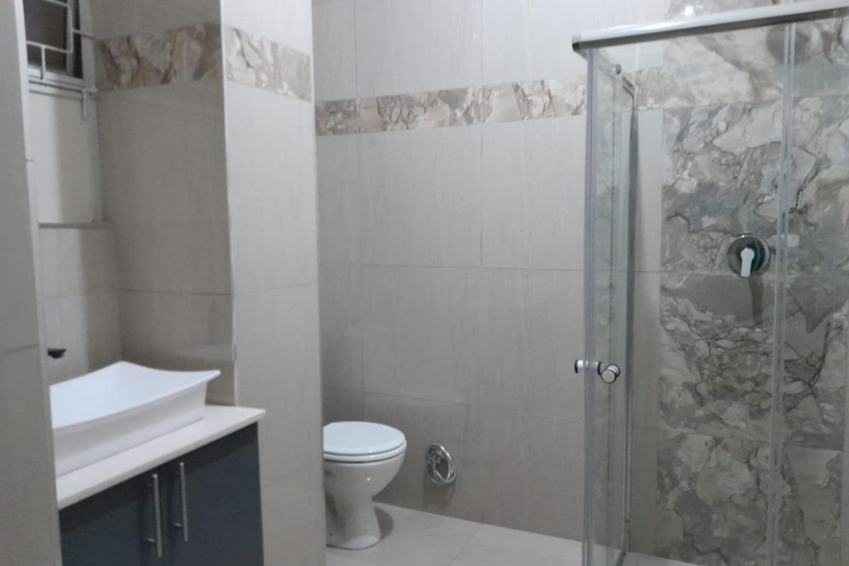 A modern bathroom featuring a vanity with a vessel sink, a toilet, and a glass-enclosed shower with decorative tiled accents.