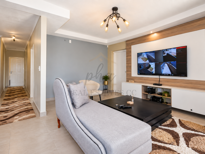 A modern living room featuring a feature wall with a built-in media console, recessed ceiling lighting, and neutral tiled flooring.