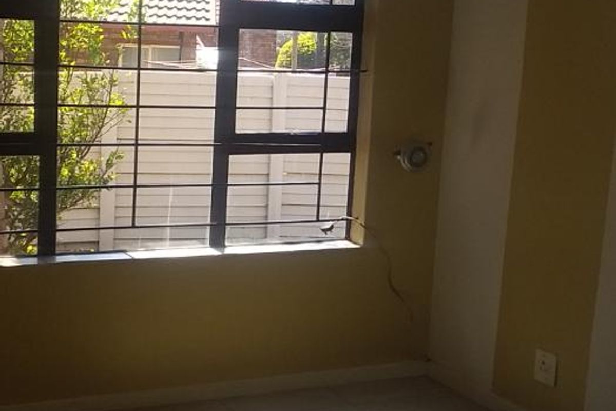 An empty bedroom featuring tiled flooring and security bars on the window, requiring minor repairs to wall surfaces and electrical fixtures.