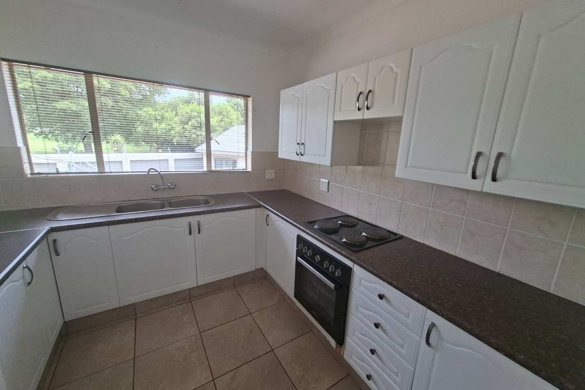 A functional kitchen featuring white cabinetry, dark laminate countertops, a built-in oven, electric hob, and tiled flooring with a large window for natural light.