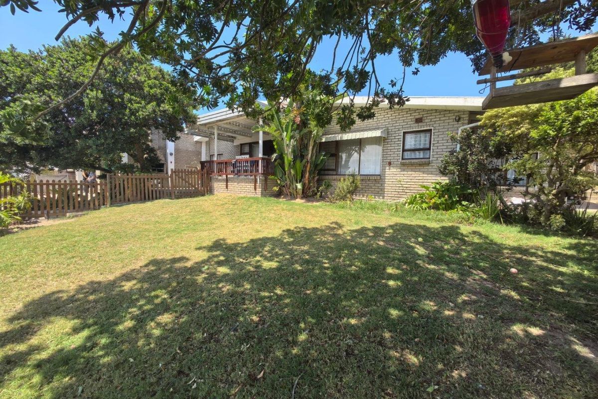A rear view of the property featuring a brick facade, a raised timber deck, and a well-maintained garden area with mature trees.
