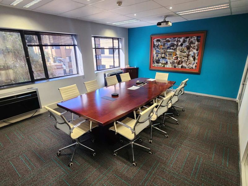 A professional boardroom or meeting room featuring a large conference table, carpeted flooring, suspended ceiling, and integrated air conditioning unit.