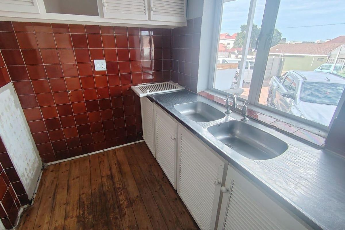 A dated kitchen area featuring a double stainless steel sink, tiled splashbacks, and white louvered cabinetry with wood-look flooring.