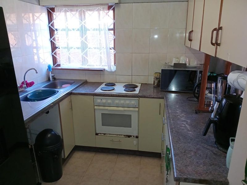 A functional kitchen featuring built-in cabinetry, laminate countertops, a stainless steel double sink, and a built-in electric stove and oven combination.