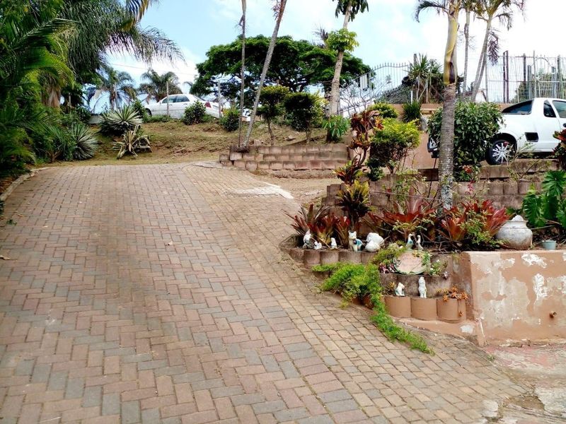 A paved driveway leading up to the property, featuring tiered garden beds with retaining walls and established landscaping.