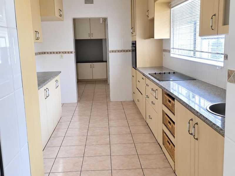 A functional galley-style kitchen featuring light wood cabinetry, granite countertops, built-in oven, electric cooktop, and tiled flooring, with an adjacent scullery area.