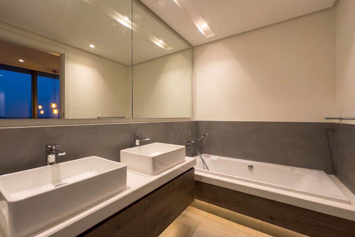Modern bathroom featuring a double vanity with vessel sinks, a built-in bathtub, large wall mirror, and elegant recessed and under-cabinet lighting.