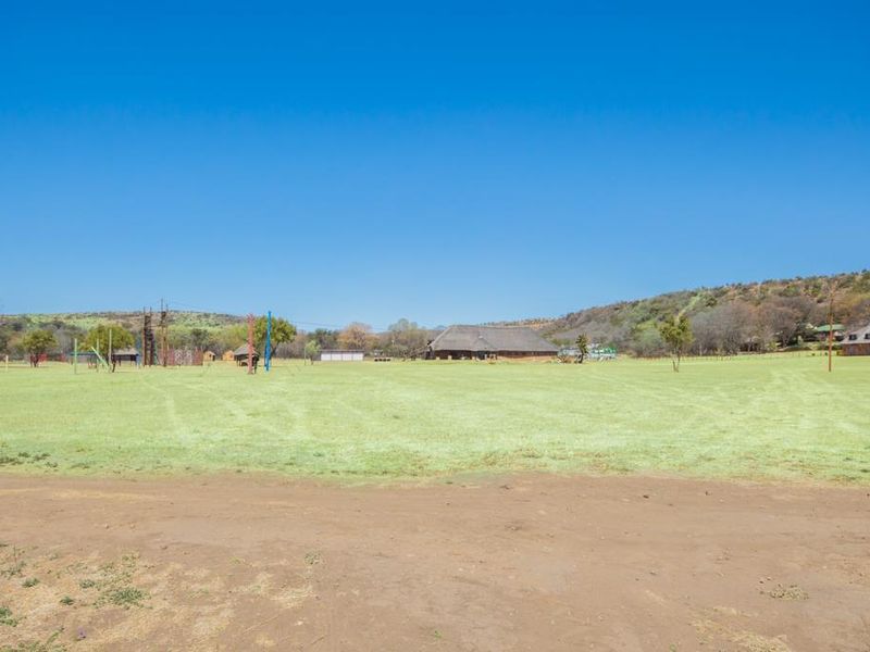 A wide-angle view of the expansive farm grounds featuring open grassy fields, scattered structures, and a clear blue sky.