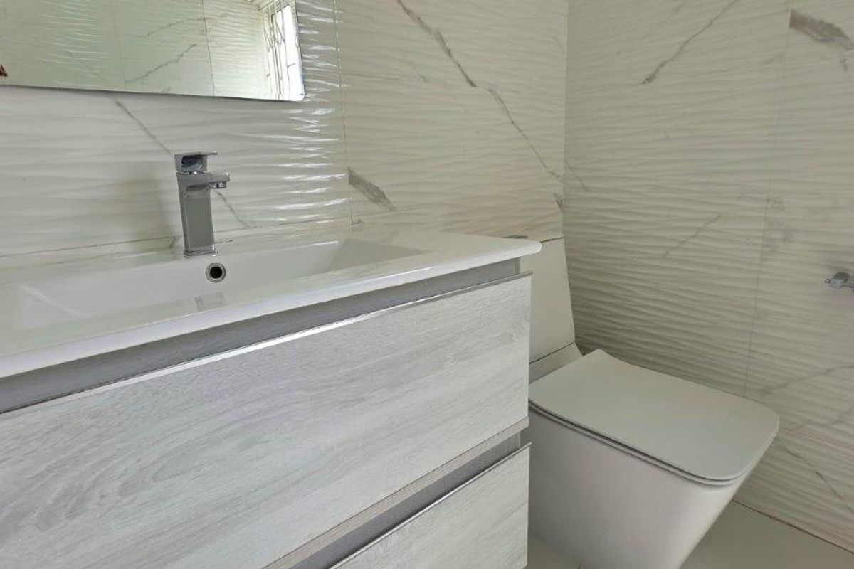 A modern bathroom featuring a sleek vanity cabinet with a basin, a wall-mounted toilet, and contemporary textured marble-effect wall tiles.