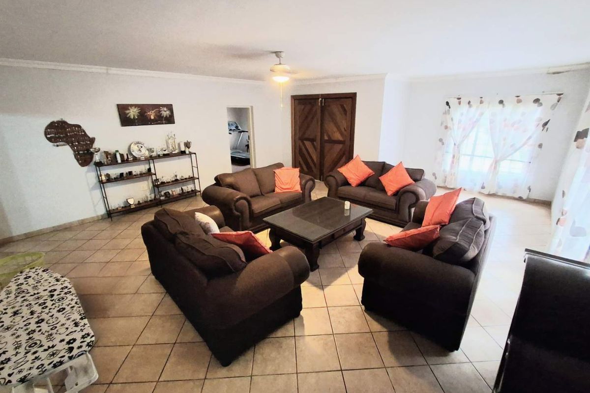 Spacious living room featuring neutral tiled flooring, a central ceiling fan, and double wooden doors leading to adjacent areas.