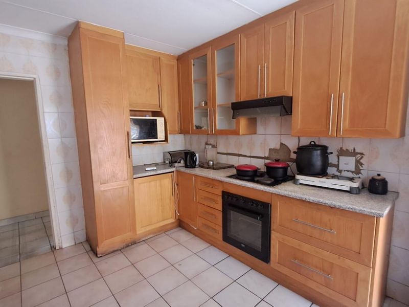A functional kitchen featuring wooden cabinetry, granite countertops, built-in oven, and hob, with tiled flooring and backsplash throughout.