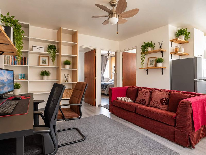 An open-plan living area featuring built-in shelving, a ceiling fan, and laminate flooring, seamlessly connecting to a functional kitchen space.