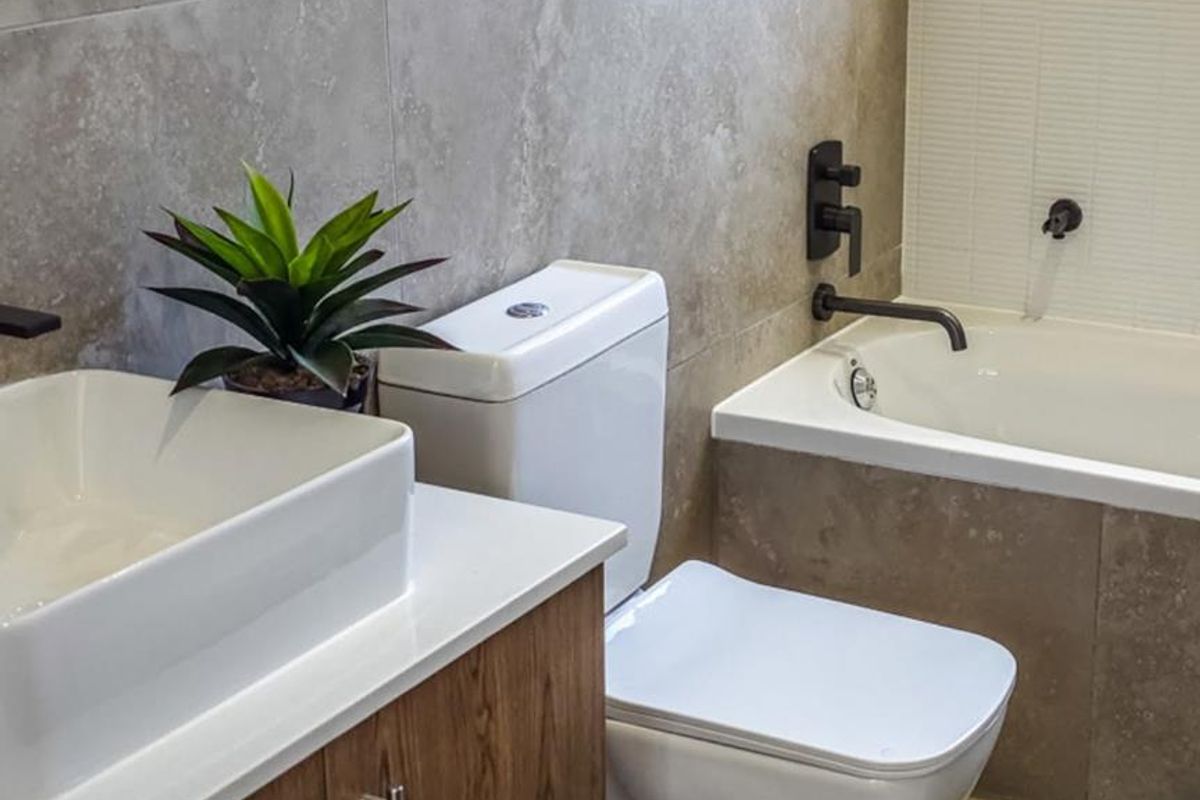 Modern bathroom featuring a wood-finish vanity with vessel sink, a white toilet, and a built-in bathtub with contemporary matte black fixtures and neutral tiling.