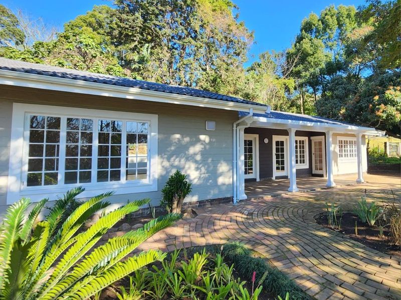 A well-maintained rear exterior view of the townhouse featuring a covered patio, brick paved pathways, and classic multi-pane windows set against a lush garden.