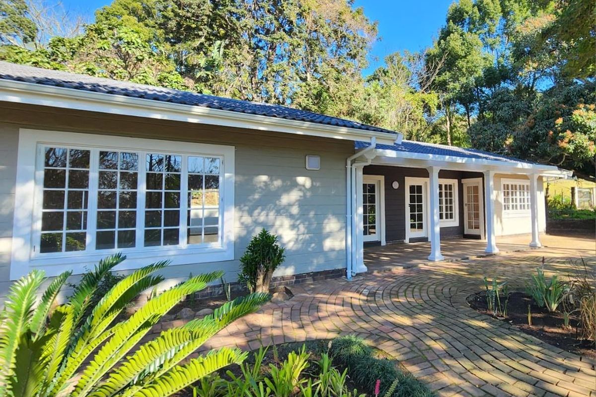 A well-maintained rear exterior view of the townhouse featuring a covered patio, brick paved pathways, and classic multi-pane windows set against a lush garden.