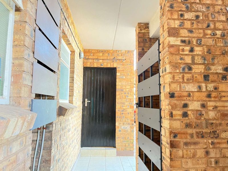A private entrance area featuring exposed brick walls, tiled flooring, and a secure entrance door with a metal security gate.