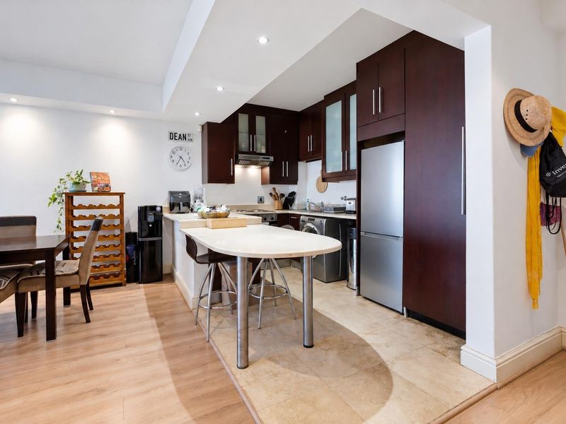 Open-plan kitchen and dining area featuring dark wood cabinetry, a stone breakfast bar, integrated appliances, and a mix of tiled and laminate flooring.