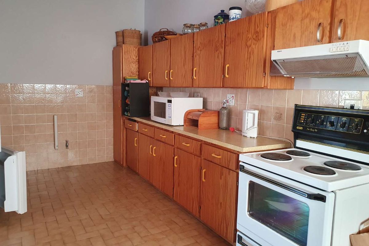A functional kitchen featuring wooden cabinetry, tiled splashbacks, and a freestanding stove with an integrated extractor fan.