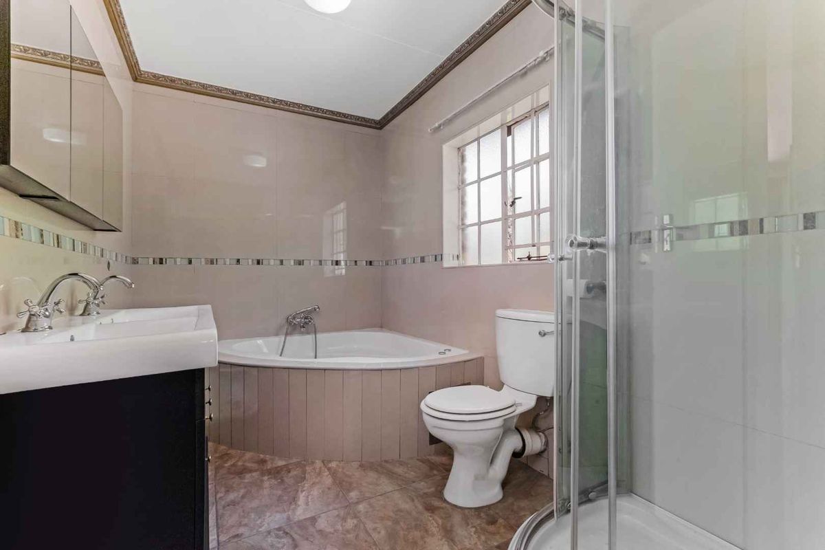 A functional bathroom featuring a corner bathtub, a separate glass-enclosed shower, a vanity basin, and a toilet with tiled flooring and walls.