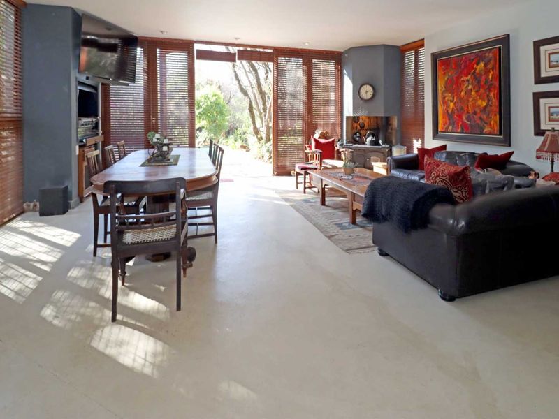 Spacious open-plan living and dining area featuring polished concrete floors, extensive timber blinds, and large sliding doors opening to the garden.