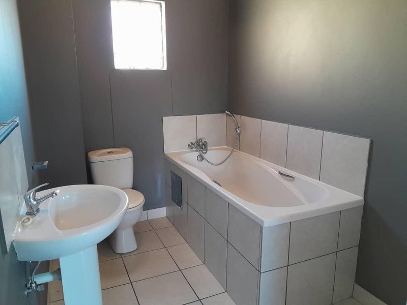 A clean, functional bathroom featuring a pedestal basin, toilet, and a tiled built-in bathtub with a handheld shower attachment.