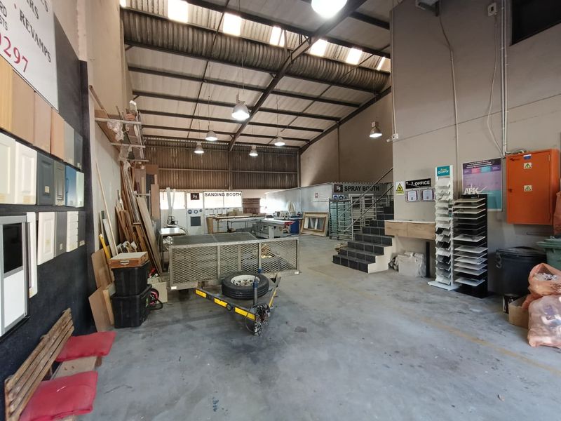 Spacious industrial workshop area featuring high ceilings, concrete flooring, and integrated utility zones including a designated sanding and spray booth.