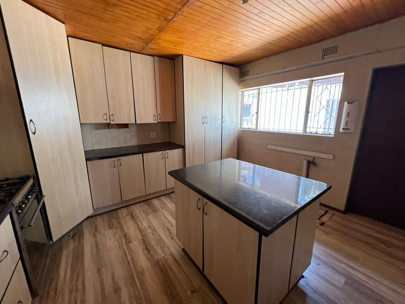A functional kitchen featuring light-toned laminate cabinetry, a central island, built-in oven, and timber-clad ceiling, offering a practical layout ready for updates.
