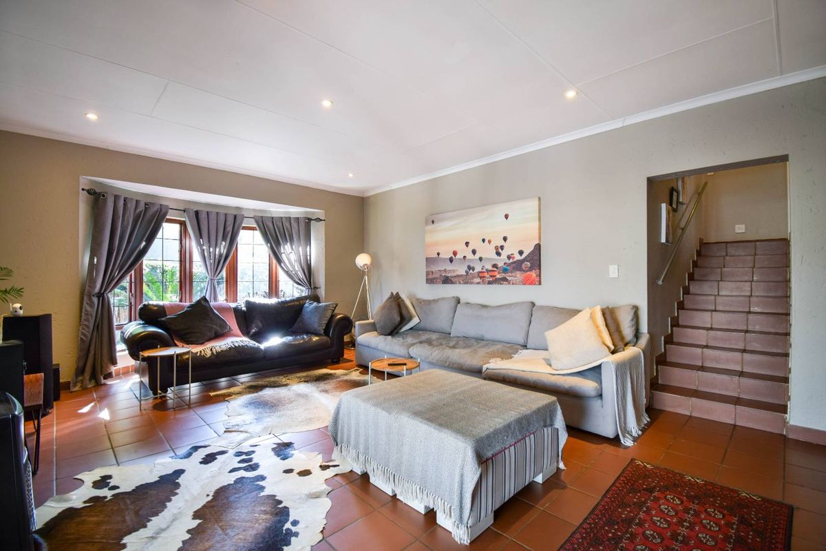 Spacious living room featuring terracotta floor tiles, recessed downlighting, and a staircase leading to the upper level.