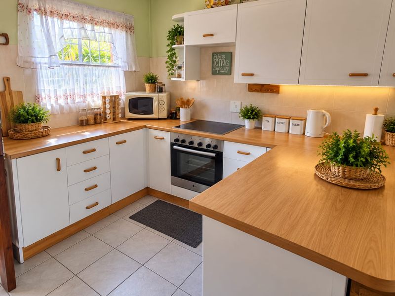 A well-maintained kitchen featuring white cabinetry, wood-look laminate countertops, an integrated electric hob and oven, and tiled flooring with under-cabinet lighting.