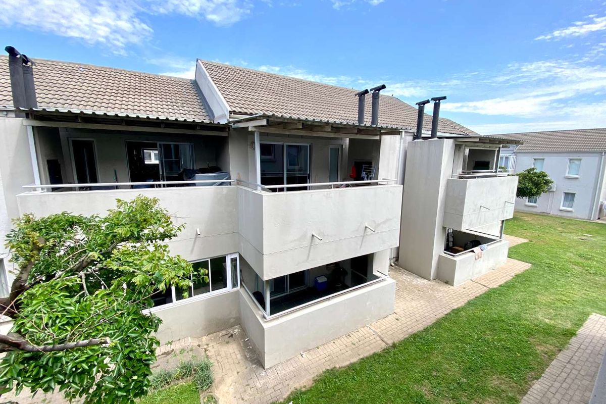 Rear view of a multi-story apartment complex featuring private balconies, sliding glass doors, tiled roofing, and a shared garden area with paved walkways.