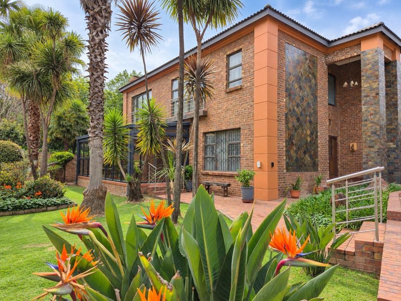 A well-maintained double-story face brick home featuring a slate tile accent wall, paved patio area, and established landscaped garden.