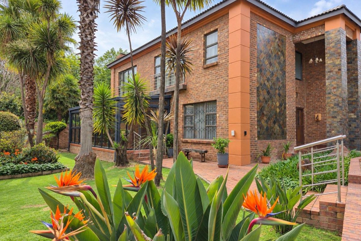 A well-maintained double-story face brick home featuring a slate tile accent wall, paved patio area, and established landscaped garden.