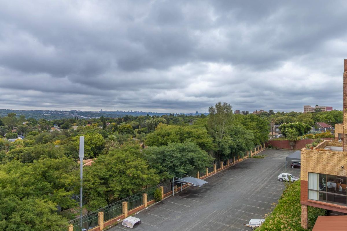 Elevated aerial view overlooking the office property's parking area, perimeter fencing, and surrounding lush green landscape with a distant city skyline.