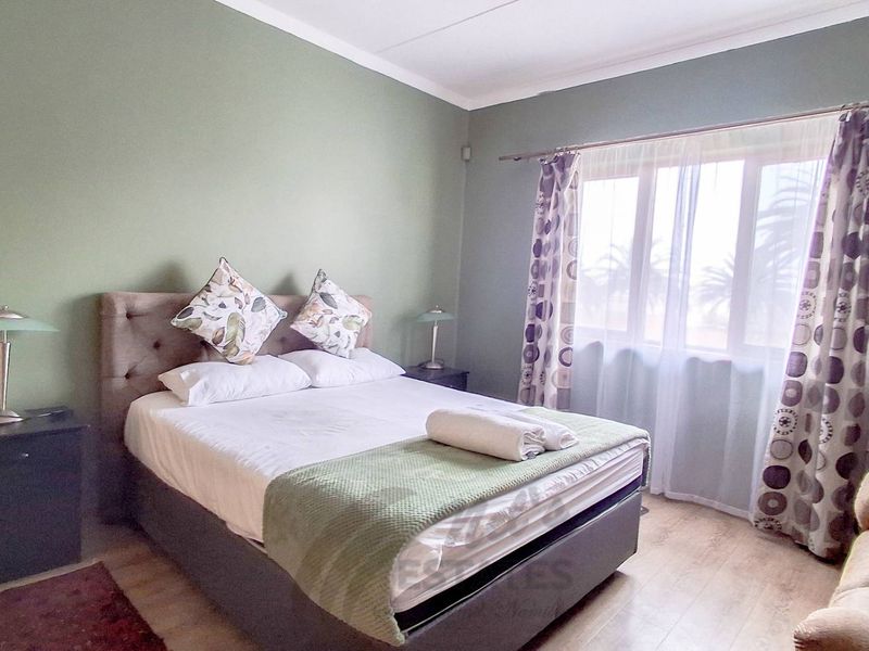 A bedroom featuring laminate flooring and a large window with a curtain rod, providing natural light.
