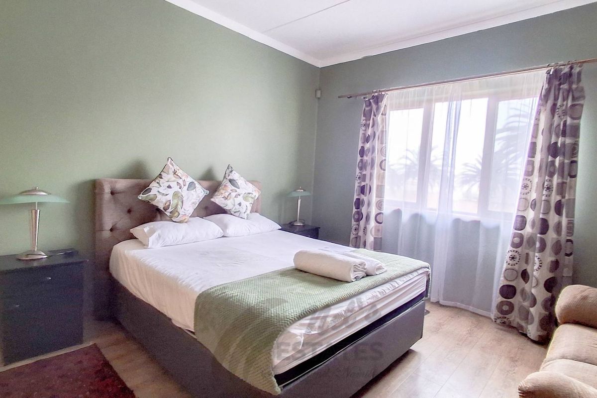 A bedroom featuring laminate flooring and a large window with a curtain rod, providing natural light.