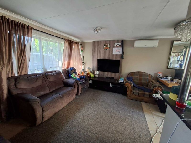 A comfortable living room featuring a wood-look feature wall, split-system air conditioning, and a combination of tiled and carpeted flooring.