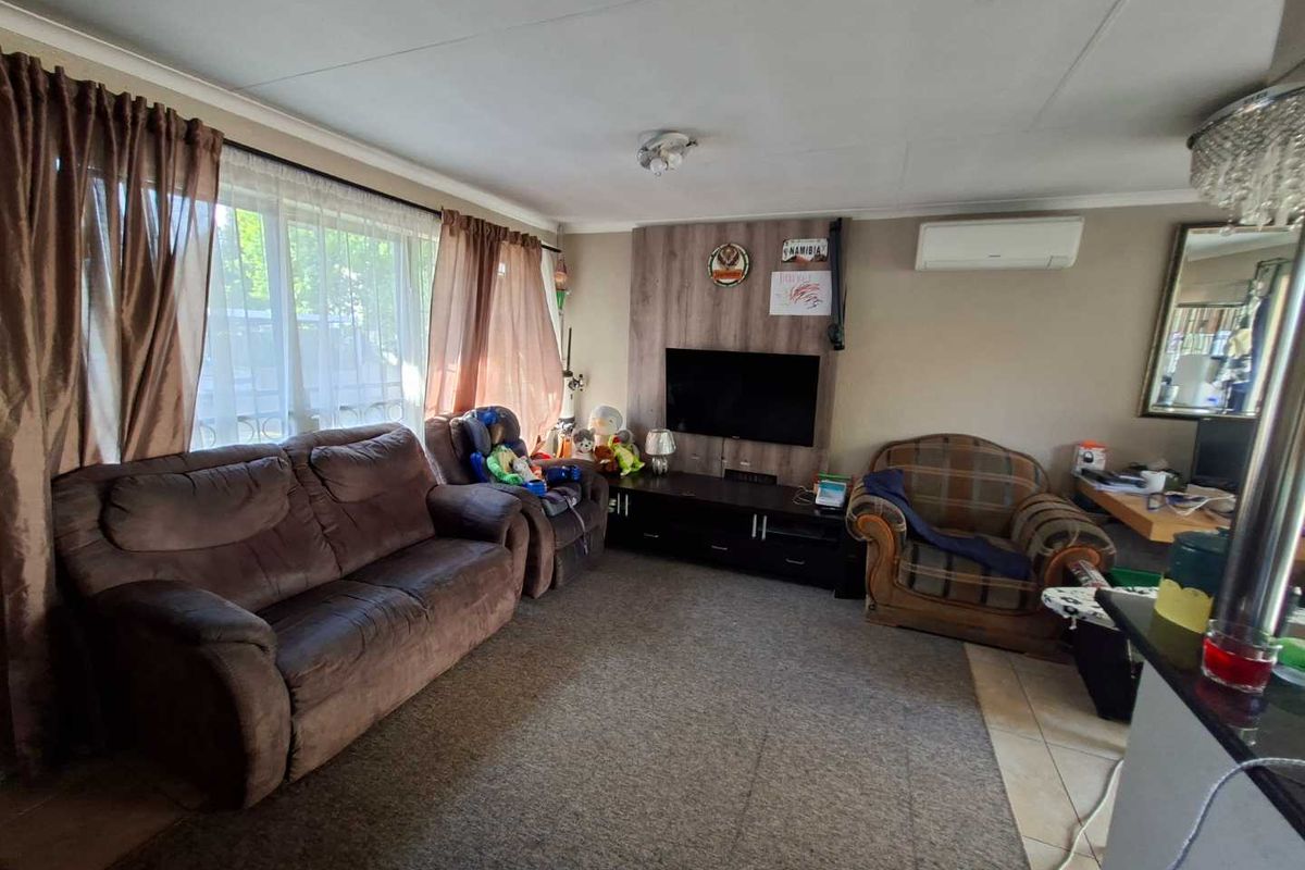 A comfortable living room featuring a wood-look feature wall, split-system air conditioning, and a combination of tiled and carpeted flooring.