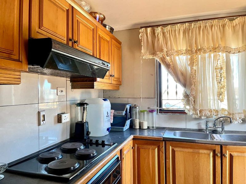 A functional kitchen featuring traditional wooden cabinetry, a built-in electric hob with extractor fan, and a stainless steel sink with tiled backsplash.