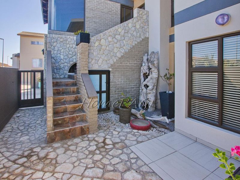 A well-maintained rear courtyard featuring stone-clad walls, a tiled staircase, and paved flooring, providing a structured and attractive outdoor transition area.