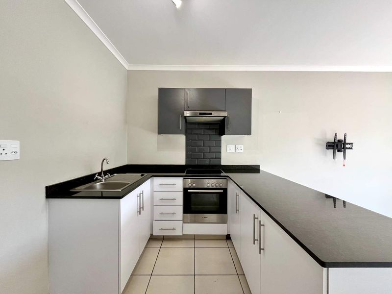 A modern, clean kitchen featuring white cabinetry, contrasting black granite countertops, a built-in oven, hob, extractor fan, and tiled backsplash.