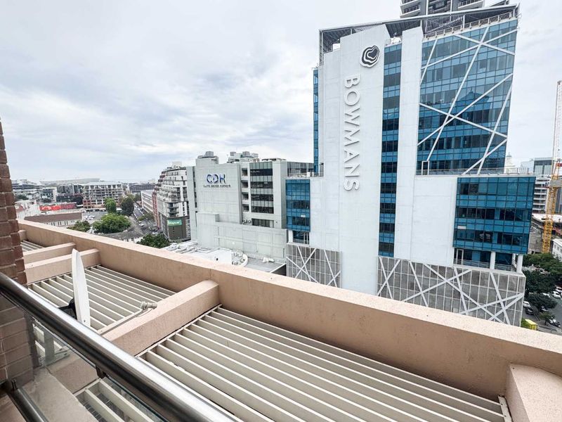 A balcony featuring a metal railing and a louvred roof, offering an elevated urban view of the surrounding office buildings.