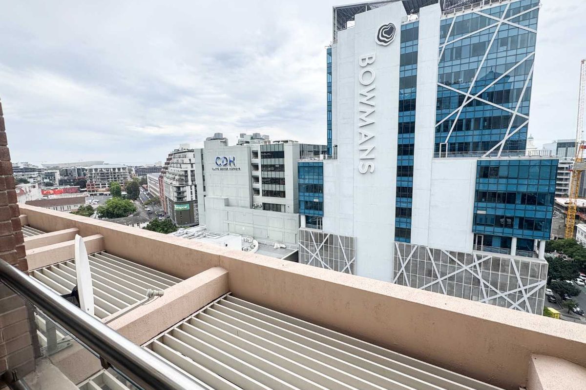 A balcony featuring a metal railing and a louvred roof, offering an elevated urban view of the surrounding office buildings.