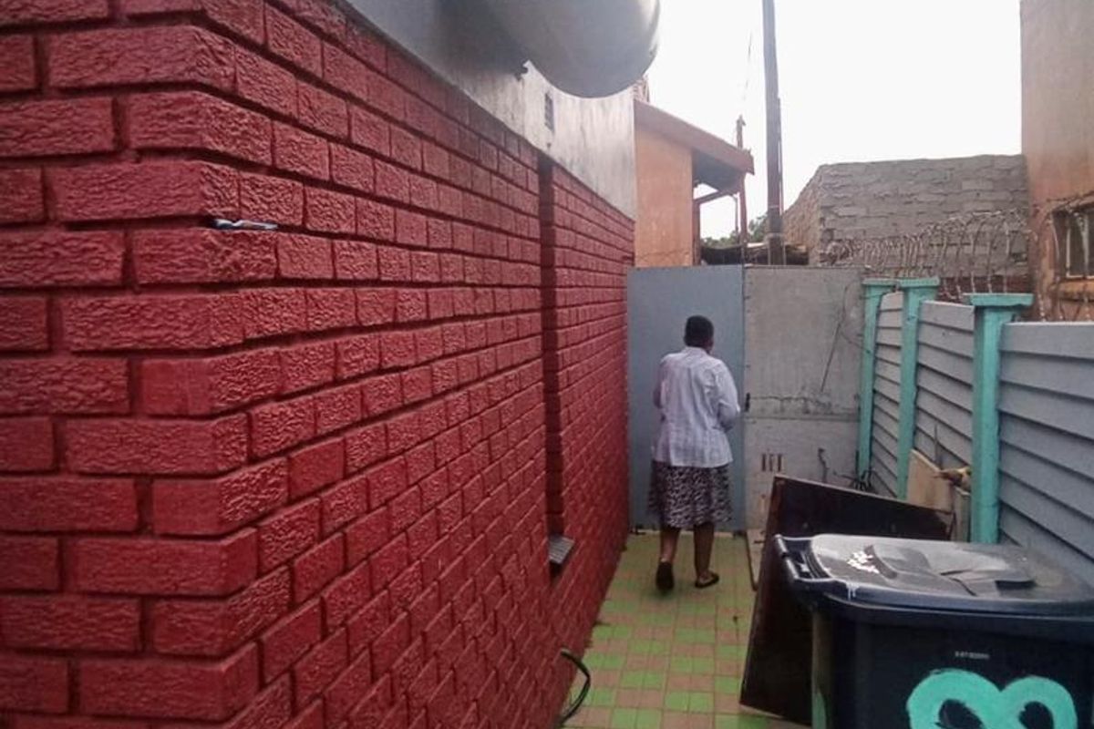 Side exterior walkway featuring red brick wall finish, paved flooring, and an externally mounted electric water heater.