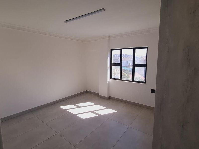 A bright, empty bedroom featuring neutral tiled flooring, clean white walls, decorative ceiling cornicing, and a large window providing natural light.
