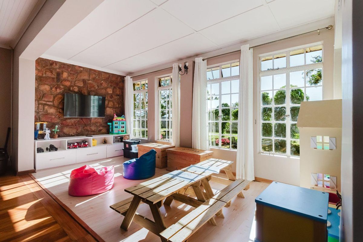 Bright living area featuring a rustic stone accent wall, timber flooring, and large multi-pane windows providing ample natural light and garden views.