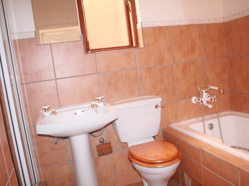 A dated bathroom featuring a pedestal basin, toilet, and built-in bathtub with wall-mounted fixtures, finished with terracotta-style wall and floor tiles.
